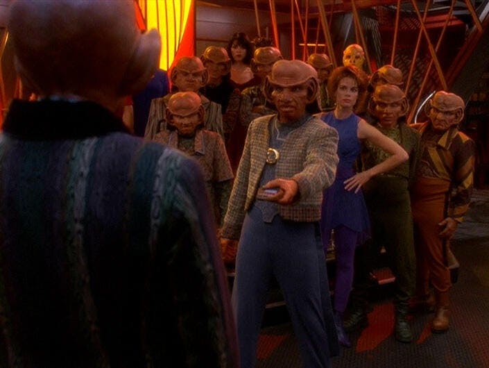 A group of Ferengi and a human woman face off on what appears to be a starship or space station set in Star Trek: Deep Space Nine