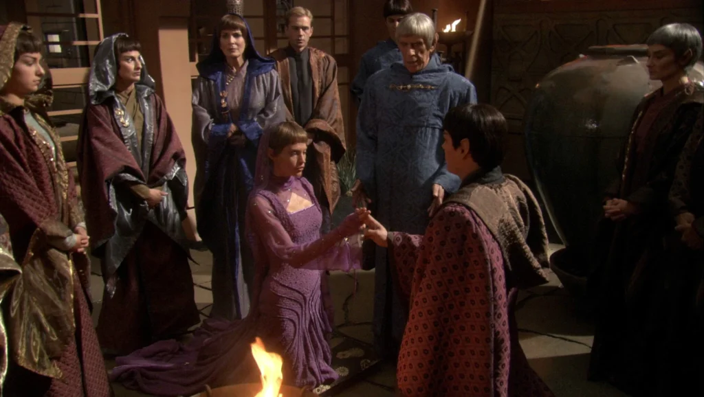 A group of Vulcans gather around a small fire during a ceremony in a dimly lit chamber.
