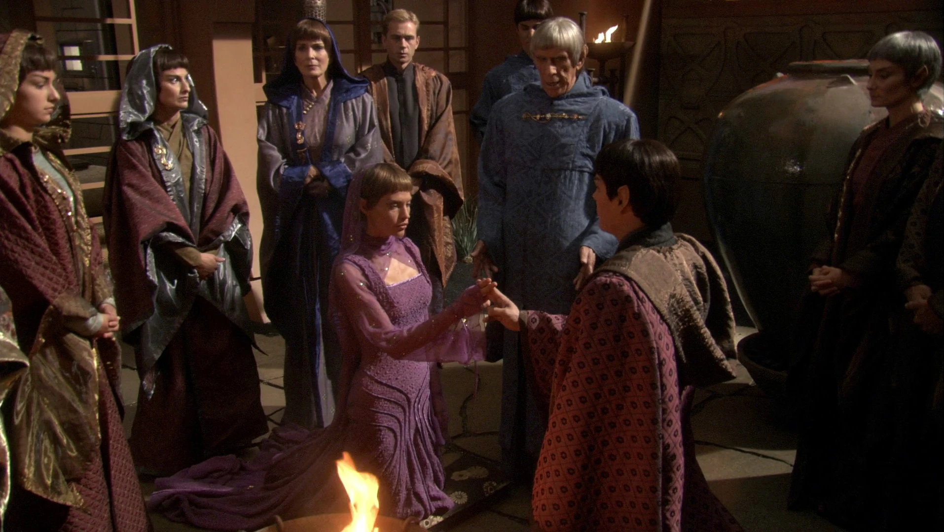 A group of Vulcans gather around a small fire during a ceremony in a dimly lit chamber.