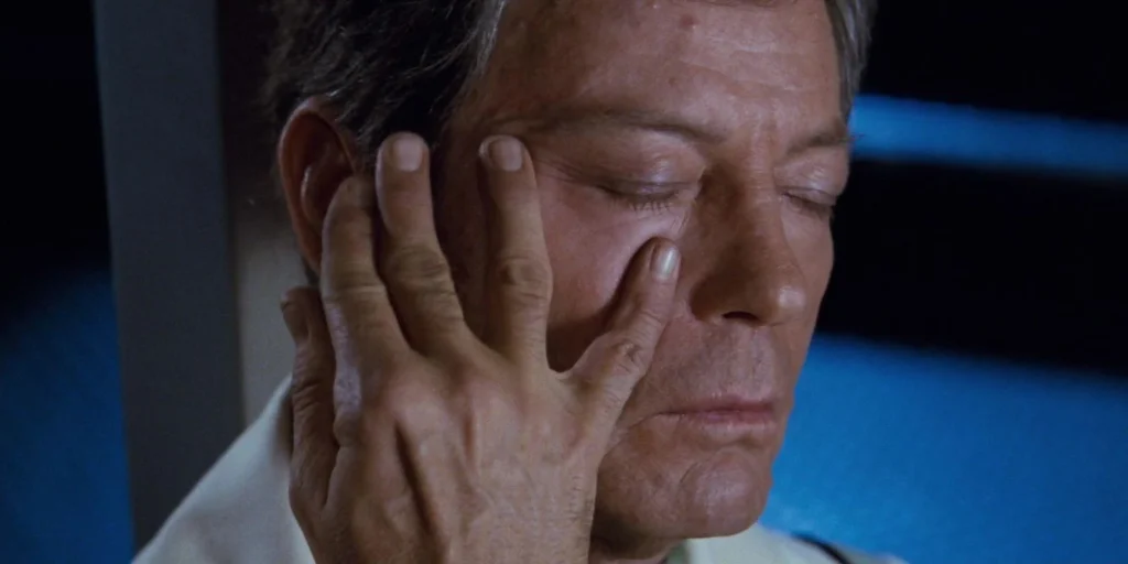 A close-up of an older man with his eyes closed as a hand presses against his face during a mind meld.
