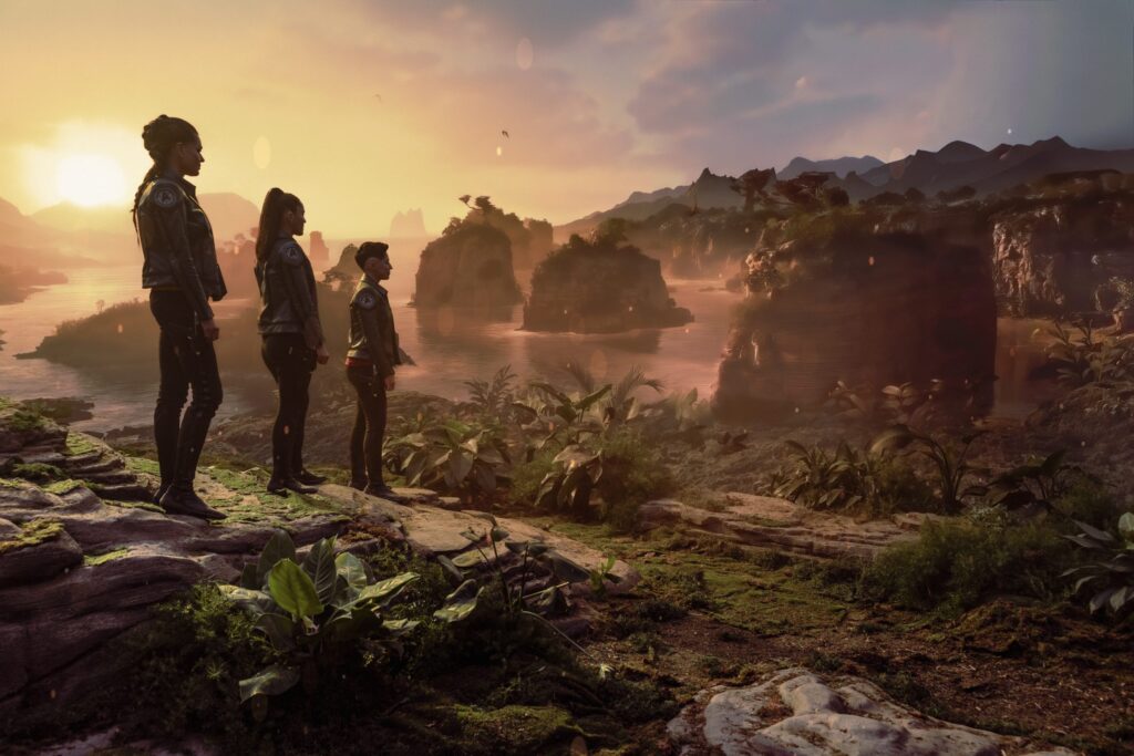 Erica Ortegas, Una Chin-Riley (Number One) and La'an Noonien-Singh standing on a rock cliff looking over earth 65 million years ago as it is dusty and green with dinosaurs walking about from Star Trek: Strange New Worlds season four episode one Valles Marineris.