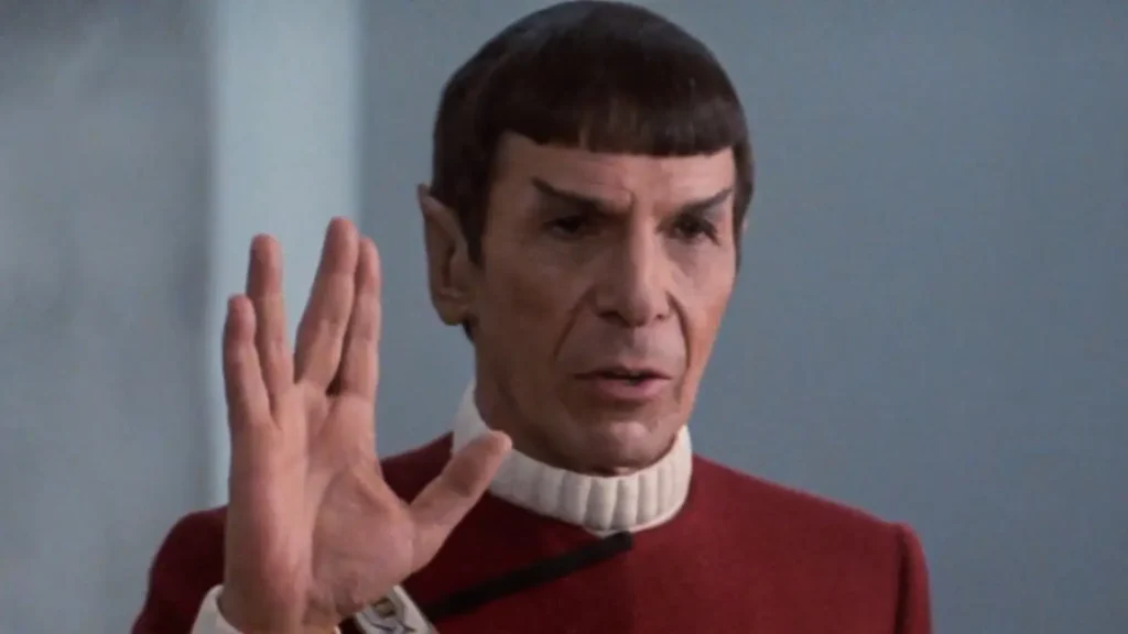 An elderly Vulcan officer in a red Starfleet uniform gives the traditional Vulcan salute.