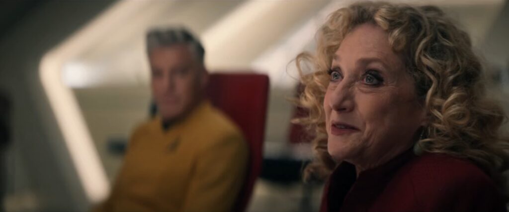Commander Pelia, a female Lanthanite Starfleet officer speaking to the table in the ready room with Pike in the background from Star Trek: Strange New Worlds season four episode one Valles Marineris.